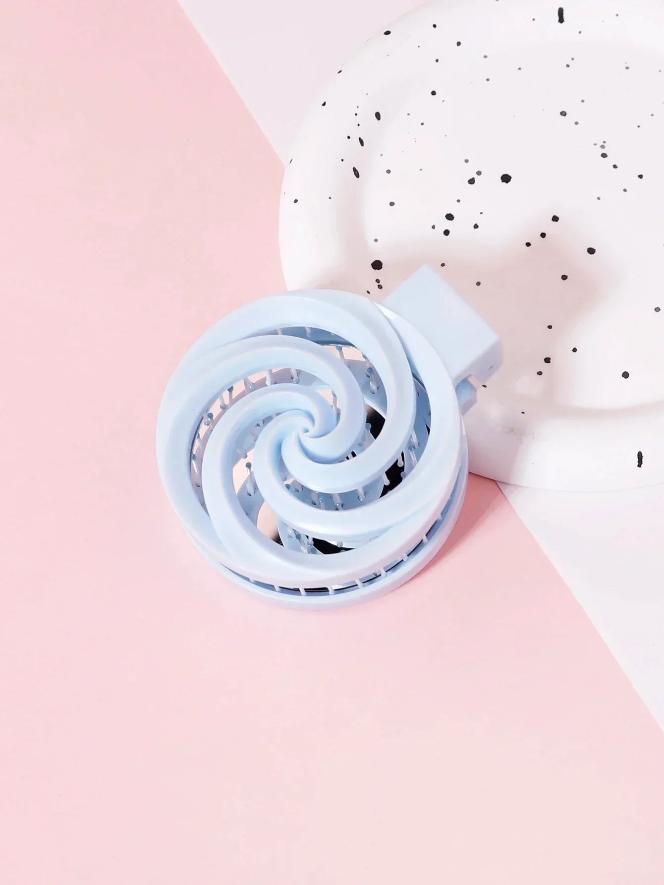 Brosse à cheveux de voyage bleue en plastique posée sur surface rose à cÎté d'assiette blanche à motifs noirs