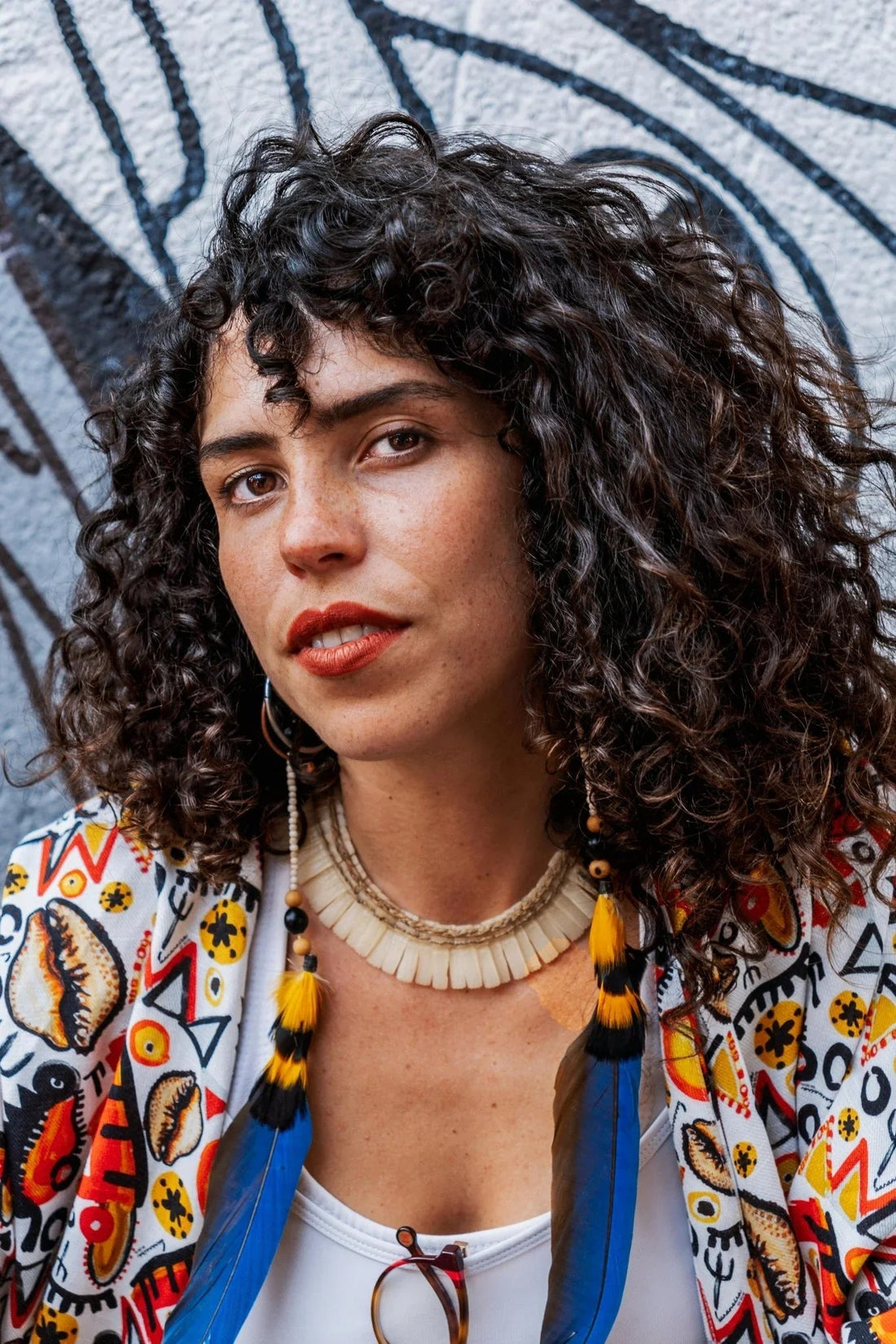 Portrait d'une femme aux cheveux bouclés avec plumes colorées et veste à motifs colorés