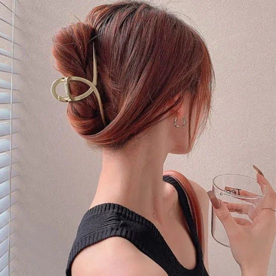 Femme de profil coiffée d'une pince à cheveux métal doré, tenant un verre, fond mur clair