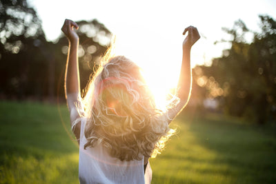 Femme de dos avec beaux cheveux les mains en l'air et sous rayons de soleil