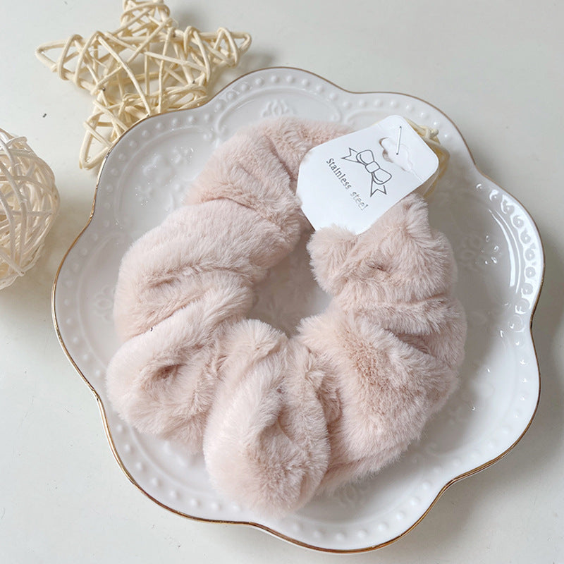 Chouchou en fausse fourrure crème beige posé sur une assiette blanche décorative, présentation élégante du produit.