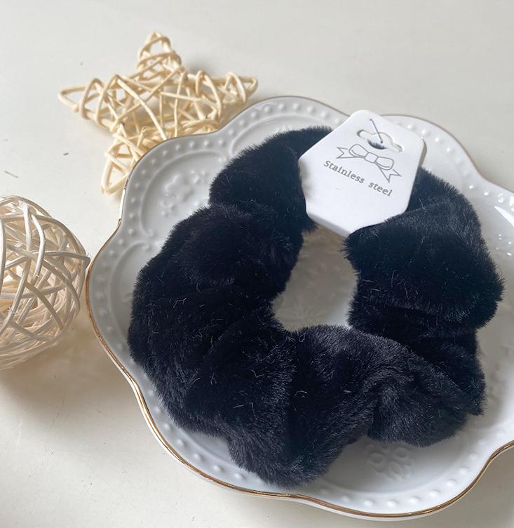 Chouchou en fausse fourrure noir posé sur une assiette blanche décorative, présentation élégante du produit.