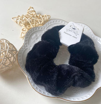 Chouchou en fausse fourrure noir posé sur une assiette blanche décorative, présentation élégante du produit.