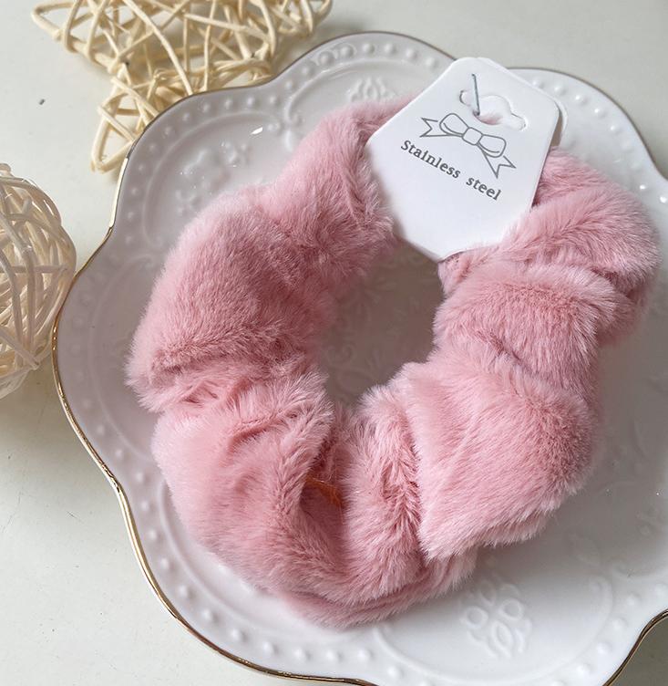 Chouchou en fausse fourrure rose pastel posé sur une assiette blanche décorative, présentation élégante du produit.