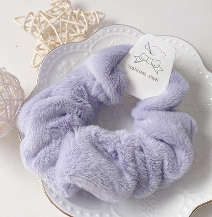 Chouchou en fausse fourrure violet clair posé sur une assiette blanche décorative, présentation élégante du produit.