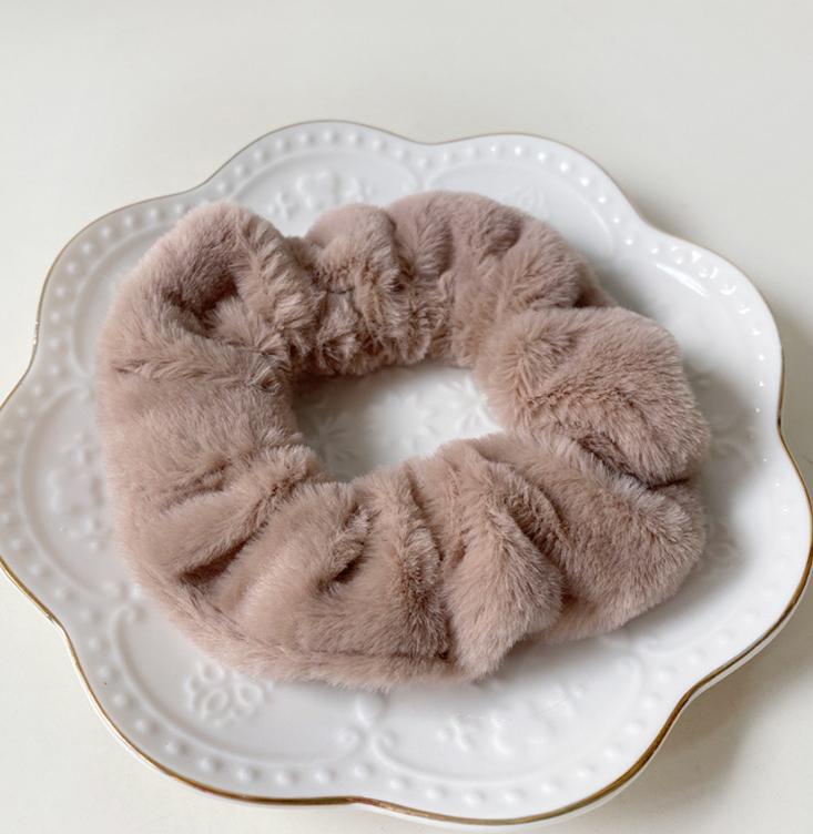 Chouchou en fausse fourrure marron clair posé sur une assiette blanche décorative, présentation élégante du produit.