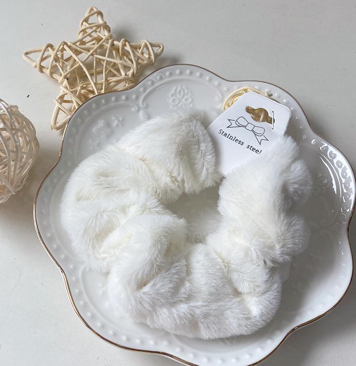 Chouchou en fausse fourrure blanc posé sur une assiette blanche décorative, présentation élégante du produit.