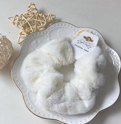 Chouchou en fausse fourrure blanc posé sur une assiette blanche décorative, présentation élégante du produit.