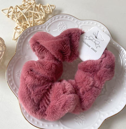 Chouchou en fausse fourrure rouge posé sur une assiette blanche décorative, présentation élégante du produit.