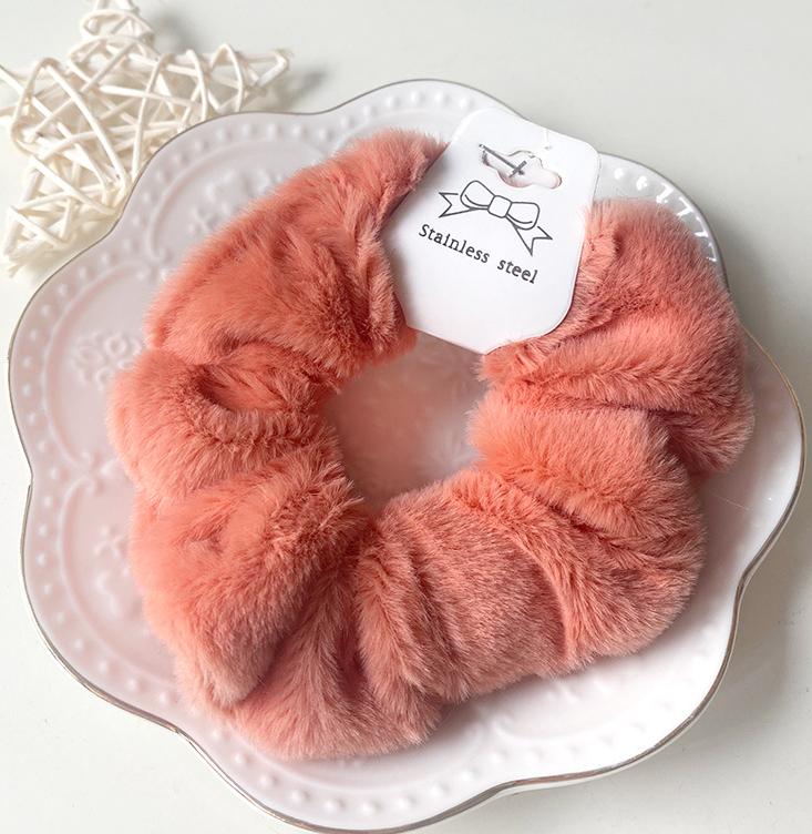 Chouchou en fausse fourrure orange posé sur une assiette blanche décorative, présentation élégante du produit.