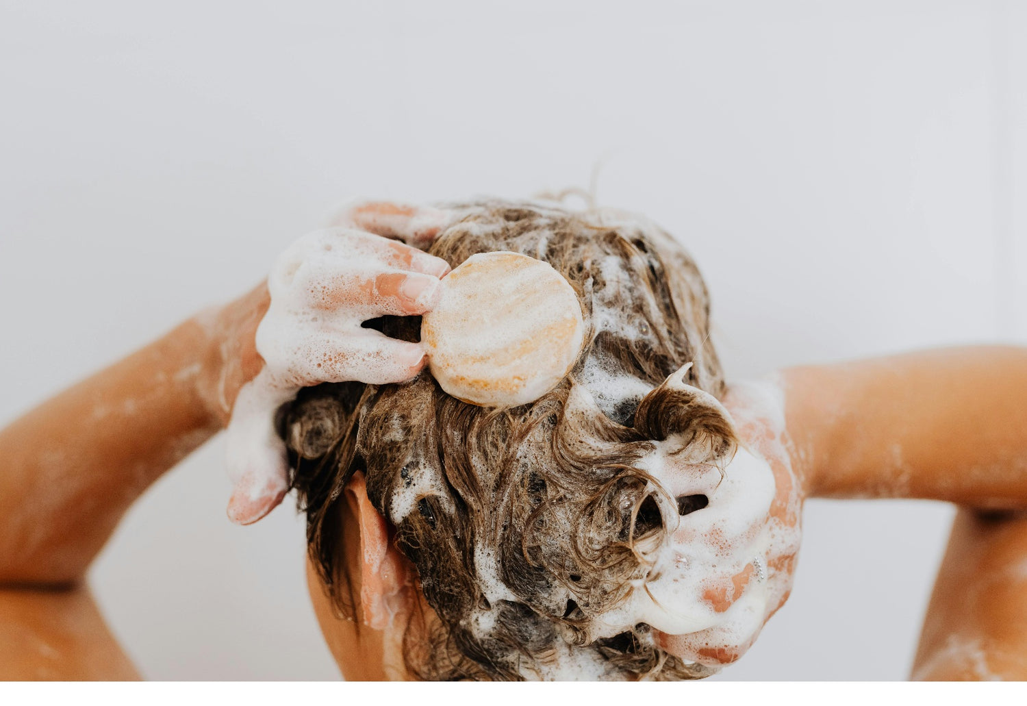 Personne lavant ses cheveux avec un shampoing solide naturel, illustrant un soin capillaire doux et écologique – CheveuSoyeux